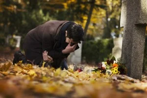 Mid adult man with flowers and candles visiting graves at the cemetery.